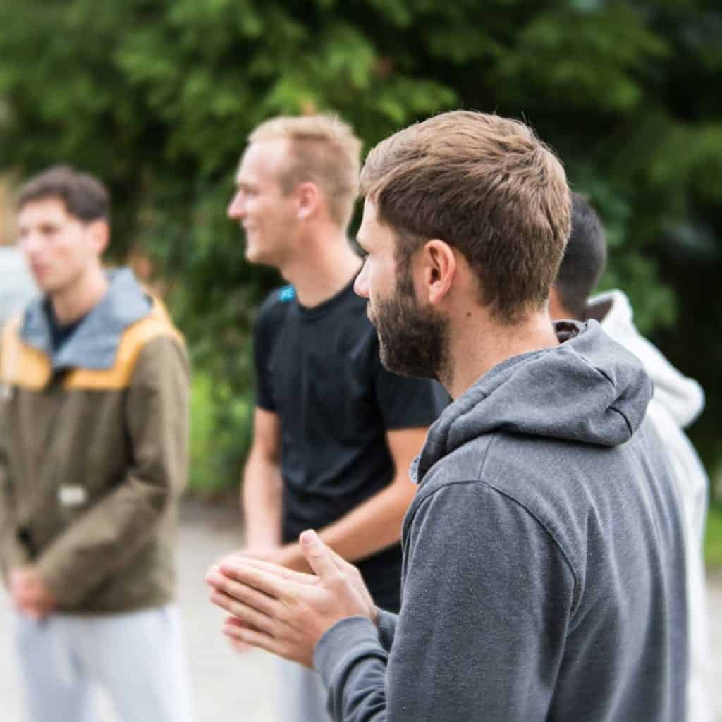 Group of men standing outside in a circle facing one another.